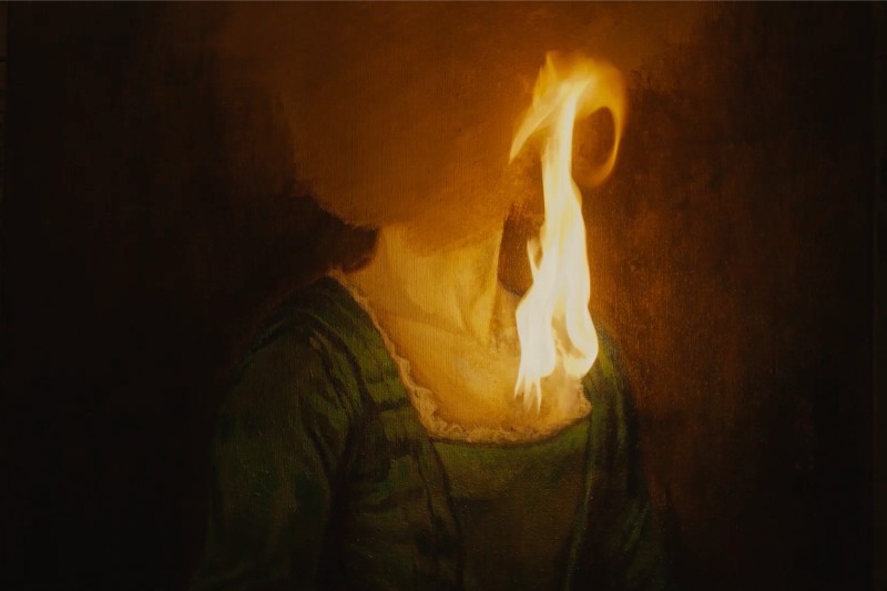 Portret kobiety w zielonej sukience w stylu klasycznym, z twarzą zasłoniętą płomieniami, co tworzy dramatyczny i surrealistyczny efekt na ciemnym tle.