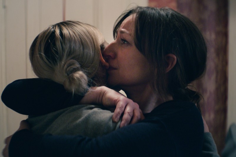 Dwie kobiety obejmują się blisko. Jedna z nich wygląda na wzruszoną, jej oczy są pełne łez, gdy mocno trzyma drugą. Scena sugeruje pocieszenie lub wsparcie w chwili rozpaczy.