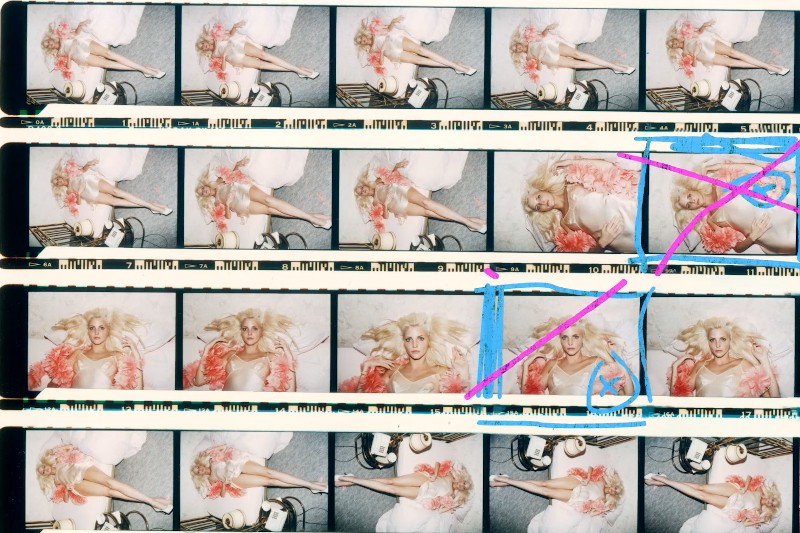 Arkusz kontaktowy przedstawiający kobietę w kwiecistej sukience pozującą na łóżku. Niektóre ramki są oznaczone niebieskimi i różowymi liniami oraz X-ami, wskazującymi na wybór lub odrzucenie. Kobieta ma blond włosy i leży w różnych pozach.