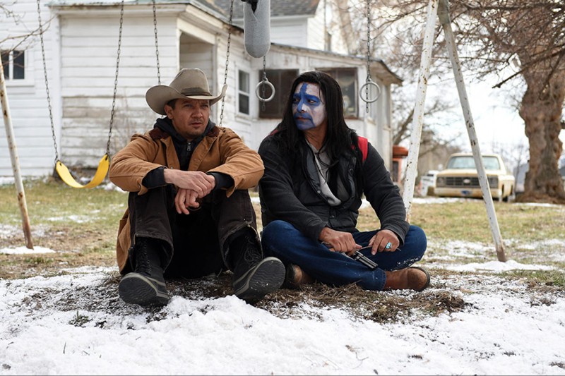 Dwóch mężczyzn siedzi na zaśnieżonym gruncie pod huśtawką. Jeden nosi kowbojski kapelusz i brązową kurtkę; drugi ma długie włosy, czarny płaszcz i niebiesko-białą farbę na twarzy. W tle widać biały dom i zaparkowaną ciężarówkę.
