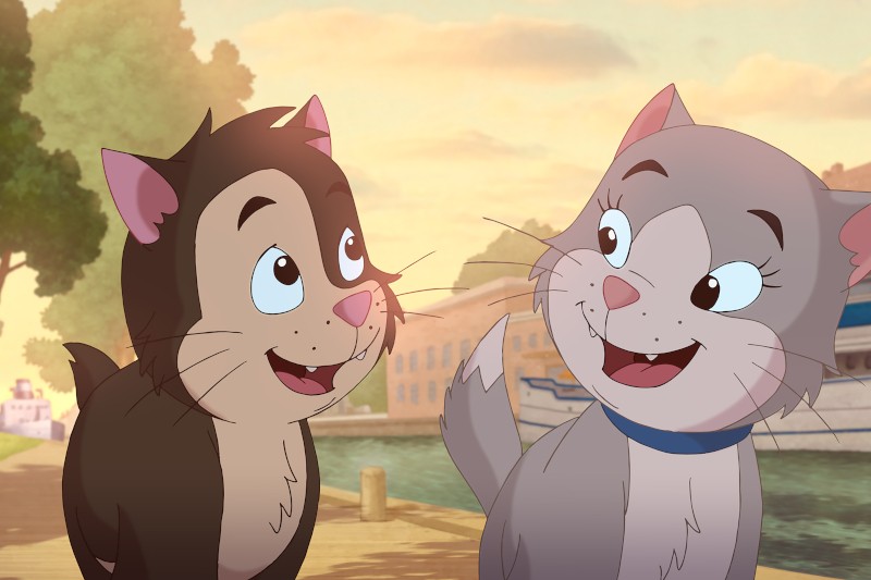 Dwa animowane koty, jeden brązowy z różowymi uszami, a drugi szary z niebieską obrożą, uśmiechają się do siebie na pomoście nad wodą, na tle drzew i łodzi o zachodzie słońca.