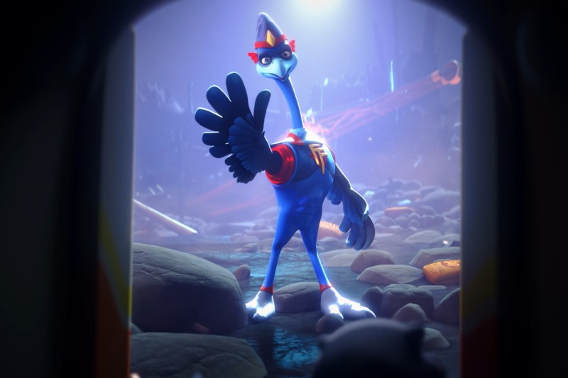 Kreskówkowy struś ubrany w kostium i maskę superbohatera pewnie stoi z jedną ręką uniesioną do góry, otoczony skałami i gruzem, w słabo oświetlonym, przypominającym jaskinię otoczeniu.