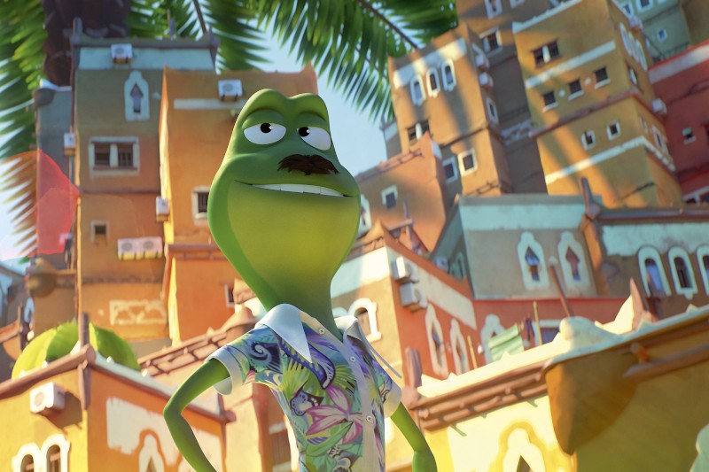 Pewna siebie zielona żaba z kreskówek z wąsami i kolorową koszulką stoi na zewnątrz, uśmiecha się, na tle wysokich, jaskrawo kolorowych budynków i liści palmowych pod słonecznym niebem.