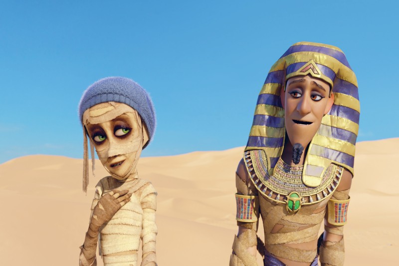 Dwie animowane mumie stoją na pustyni. Jedna nosi niebieską czapkę i bandaże pokrywające jej ciało, podczas gdy druga nosi pasiasty faraonowy nakrycie głowy i ozdobny kołnierz. Obie mają zrelaksowane miny pod błękitnym niebem.