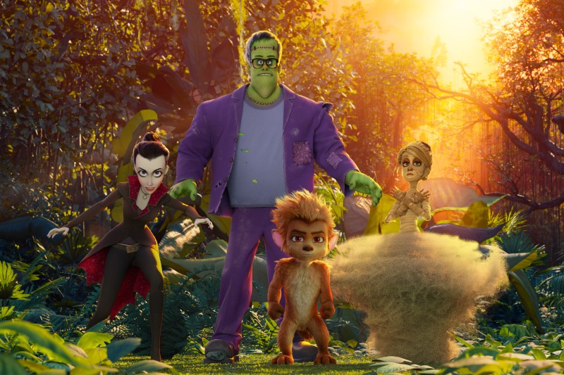 Cztery animowane postacie potworów — dziewczyna-wampir, potwór Frankensteina, dziecko-wilkołak i mumia — stoją razem w bujnej, zielonej dżungli, a przez drzewa przebijają się promienie słońca.