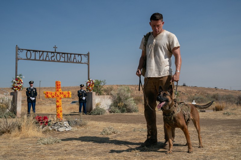 Mężczyzna w białej koszuli stoi z psem przed grobem oznaczonym pomarańczowym krzyżem, nad którym widnieje napis Camposanto. W tle stoją trzej umundurowani żołnierze. Scena rozgrywa się na zewnątrz, na suchym, trawiastym terenie.