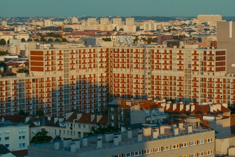 Widok z lotu ptaka na gęsto zaludnione miasto z dużymi, brązowo-białymi budynkami mieszkalnymi otoczonymi przez mniejsze budynki mieszkalne i wieżowce w oddali pod czystym niebem.