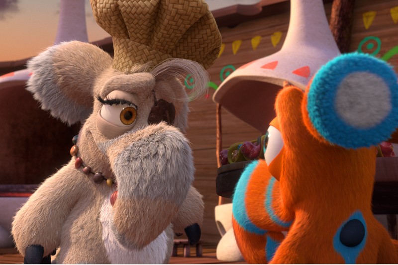 Puszyste, jasnoszare zwierzę w słomkowym kapeluszu szefa kuchni i naszyjniku poważnie patrzy na jaskrawo pomarańczowe i niebieskie stworzenie. Stoją przed chatami ozdobionymi kolorowymi wzorami.