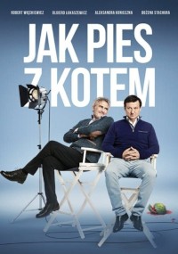 Dwóch mężczyzn siedzi na białych krzesłach reżyserskich na niebieskim tle pod tytułem „Jak Pies z Kotem”. Widoczne są światła planu filmowego i rekwizyty filmowe; jeden mężczyzna wygląda na zrelaksowanego, drugi wydaje się powściągliwy.