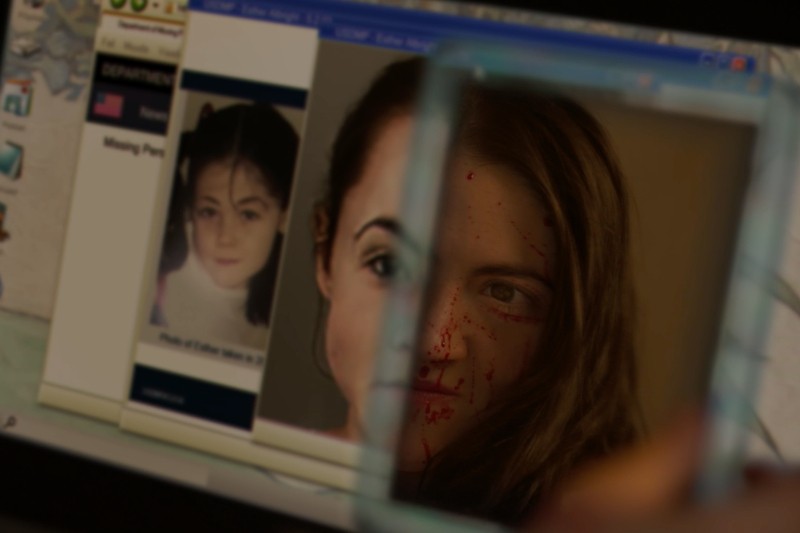 Na ekranie komputera wyświetla się zgłoszenie zaginięcia osoby, zdjęcie młodej dziewczyny obok niedawnego zdjęcia twarzy kobiety zbryzganej krwią, częściowo widocznej przez odblaskową powierzchnię.