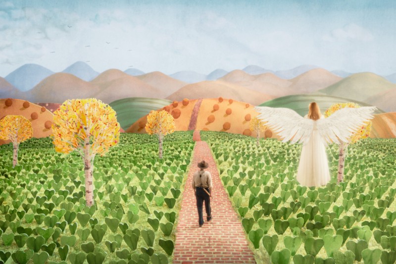 Osoba idzie ceglaną ścieżką przez zielone pole w stronę pagórków, podczas gdy postać z białymi skrzydłami i zwiewną sukienką stoi nieopodal wśród jesiennych drzew pod błękitnym niebem.