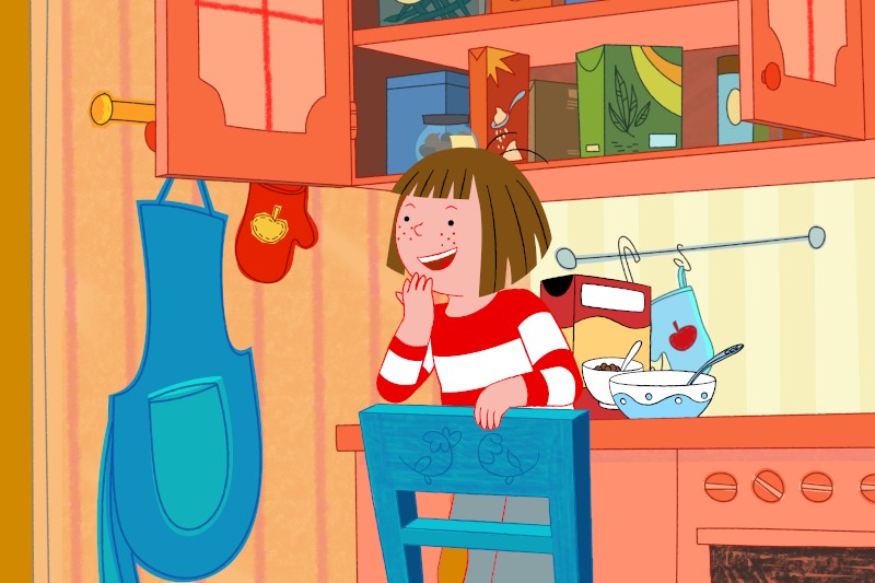 Ilustrowana postać dziewczynki z krótkimi brązowymi włosami i koszulką w czerwono-białe paski, która uśmiecha się, siedząc na niebieskim krześle w kolorowej kuchni, w tle widać przybory do pieczenia i fartuch.