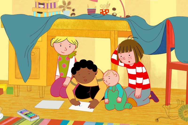 Trójka dzieci siedzi pod stołem nakrytym niebieskim obrusem, rysując na papierze. Materiały artystyczne są rozrzucone w pobliżu, a czwarte dziecko klęczy obok nich, obserwując. Scena jest kolorowa i radosna.