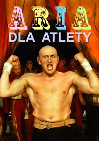 Łysy, muskularny mężczyzna w stroju cyrkowym stoi, napinając ramiona z groźnym wyrazem twarzy. Za nim artyści w kolorowych kostiumach stoją pod namiotem cyrkowym. Tekst ARIA DLA ATLETY jest wyświetlany powyżej.