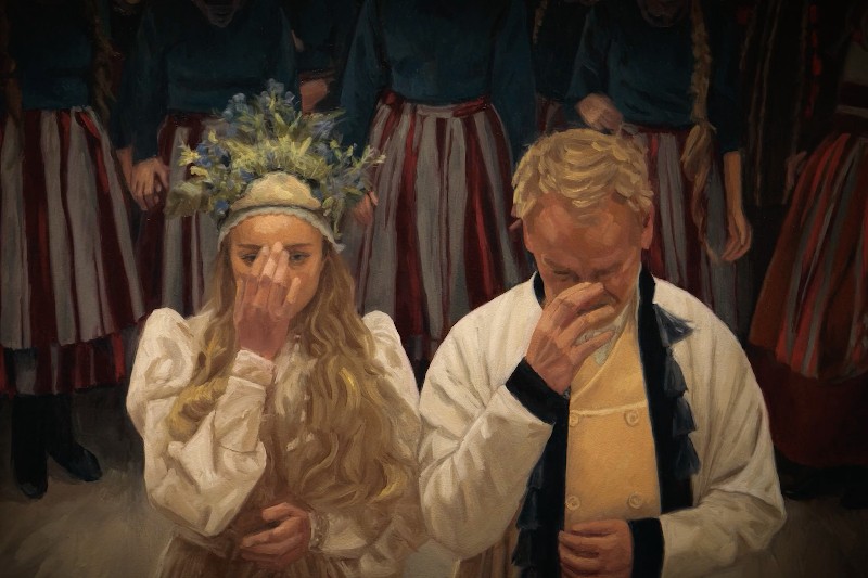 Dwie osoby w tradycyjnych strojach stoją obok siebie, każda trzymająca palce przy twarzy w pobliżu nosa. Kobieta nosi wianek z kwiatów, a kilka osób w pasiastych spódnicach stoi w tle.