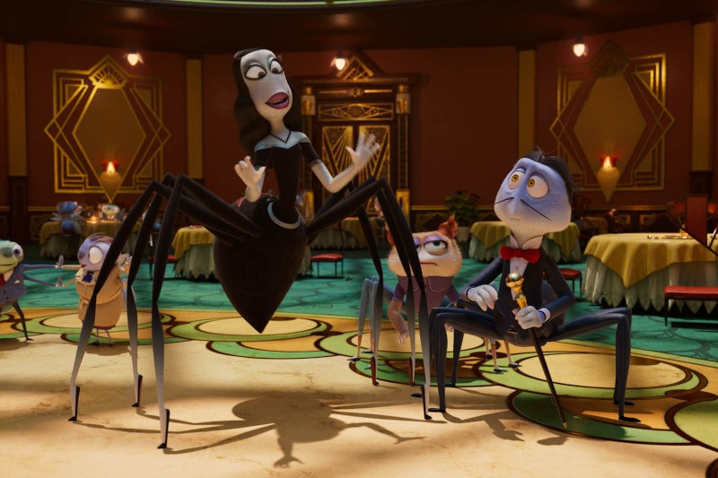 Animowane postacie pająków ubrane w formalne stroje przechadzają się w eleganckiej restauracji w stylu art déco z okrągłymi stołami i wzorzystym zielonym dywanem. Scena jest żywa i pełna życia.