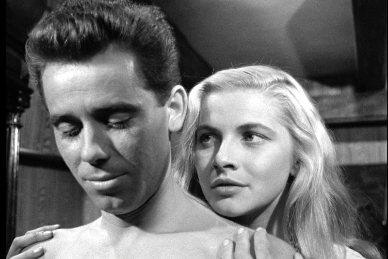 Na czarno-białym zdjęciu widać mężczyznę z zamkniętymi oczami stojącego na pierwszym planie z gołym torsem, podczas gdy za nim stoi kobieta o długich, blond włosach i patrzy na niego z poważnym wyrazem twarzy.