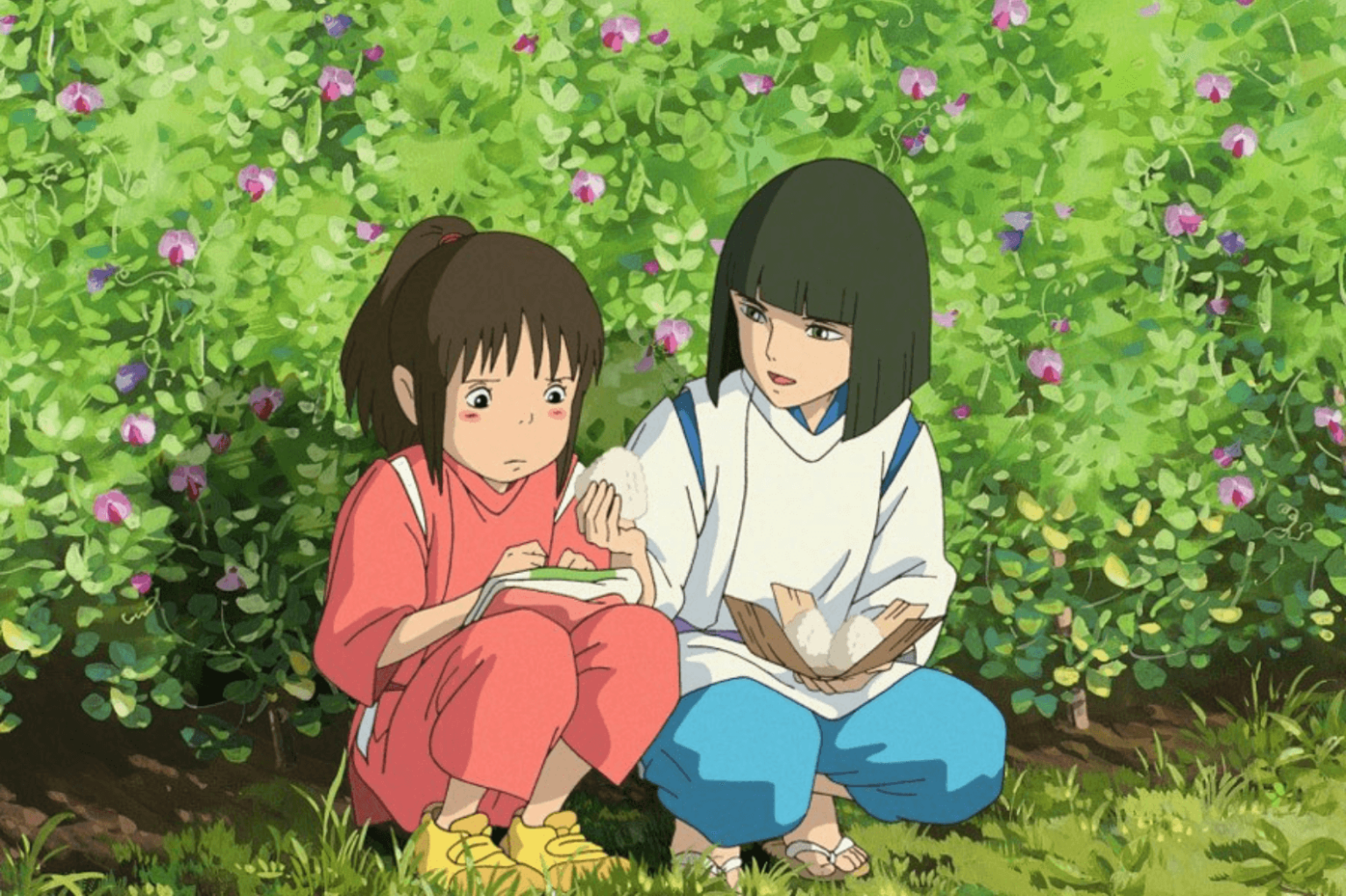 Dwie animowane postacie siedzą razem na zewnątrz, w pobliżu zielonych krzewów z różowymi kwiatami. Jedna nosi czerwony strój i wygląda nieśmiało, trzymając kulki ryżowe; druga, w bieli i błękicie, siedzi obok nich, oferując pocieszenie i jedzenie.