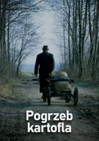 Osoba w ciemnym ubraniu i kapeluszu pcha mały wózek z workiem wzdłuż ścieżki gruntowej otoczonej nagimi drzewami. Na dole widnieje polski tekst Pogrzeb kartofla.