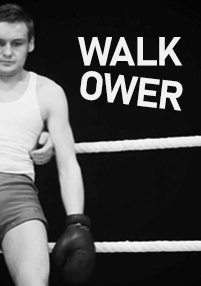 Bokser w białym podkoszulku i krótkich spodenkach siedzi na linach ringu bokserskiego, patrzy w dół, a obok niego widnieje duży napis WALK OVER.