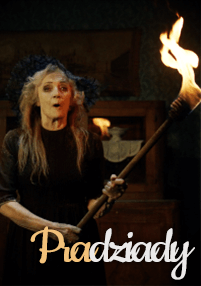 Starsza kobieta z długimi siwymi włosami trzyma płonącą pochodnię, ubrana w ciemną suknię i nakrycie głowy. Słowo Pradziady jest napisane stylizowanymi literami na dole obrazu.