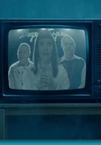 Telewizor retro wyświetla trzy osoby, dwie stojące z tyłu i jedną z przodu, wszystkie zwrócone w stronę kamery. Ekran ma niebieski odcień i ręcznie pisane pismo w tle. Telewizor stoi na drewnianej powierzchni.