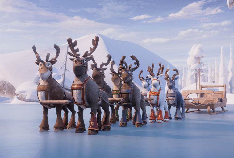 Zaprzęg animowanych reniferów w zaprzęgach, stojący na zaśnieżonym, zamarzniętym krajobrazie z drewnianymi saniami za nimi. W tle ośnieżone drzewa i góry pod częściowo zachmurzonym niebem.