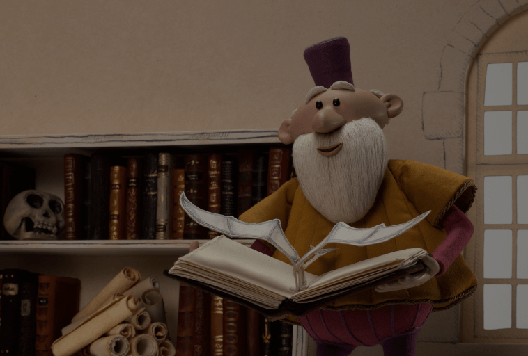 Postać w stylu claymation z białą brodą i fioletowym kapeluszem trzyma otwartą książkę ze stronami w kształcie ptaków; za nim znajdują się półki ze zwojami, starymi książkami i czaszką, obok okna.