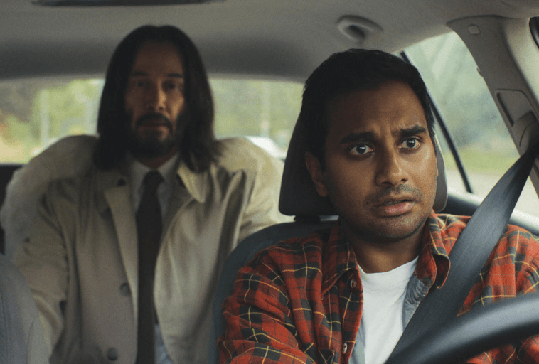 Mężczyzna z długimi włosami w beżowym płaszczu siedzi na tylnym siedzeniu samochodu, podczas gdy inny mężczyzna w czerwonej koszuli w kratę siedzi na siedzeniu kierowcy, patrząc przed siebie z zaniepokojonym wyrazem twarzy.