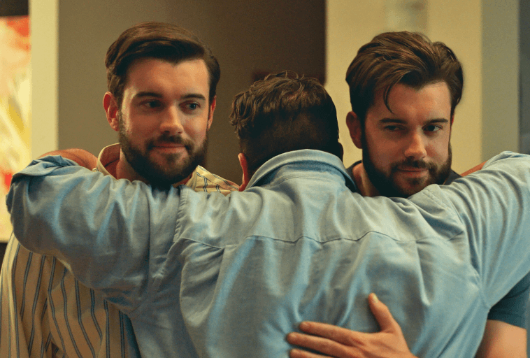Trzech mężczyzn z podobnymi brodami i ciemnymi włosami obejmuje się w grupowym uścisku. Dwóch stoi twarzą do kamery z lekkim uśmiechem, podczas gdy jeden jest odwrócony plecami. Wszyscy są ubrani w koszule z kołnierzykami w ciepło oświetlonym wnętrzu.
