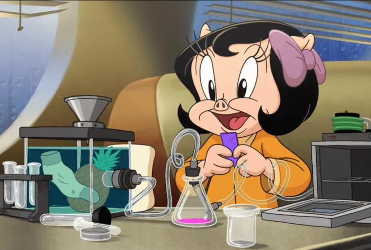 Animowana postać świni z czarnymi włosami i różową kokardą uśmiecha się podczas pracy w laboratorium. Probówki, zlewki i sprzęt naukowy znajdują się na stole; jedna kolba zawiera jasnoróżową ciecz.