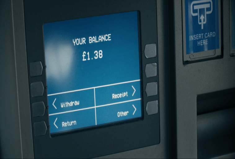 Zbliżenie ekranu bankomatu wyświetlającego saldo w wysokości 1,38 GBP, z opcjami wypłaty, zwrotu, pokwitowania i innymi. Po prawej stronie ekranu widoczne jest gniazdo karty i znak Włóż kartę.